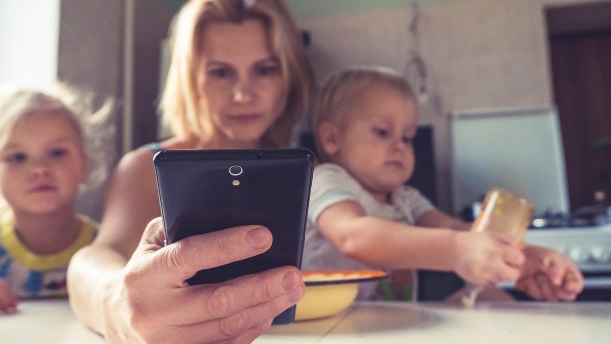 A woman uses smartphone while sitting with children, working mom